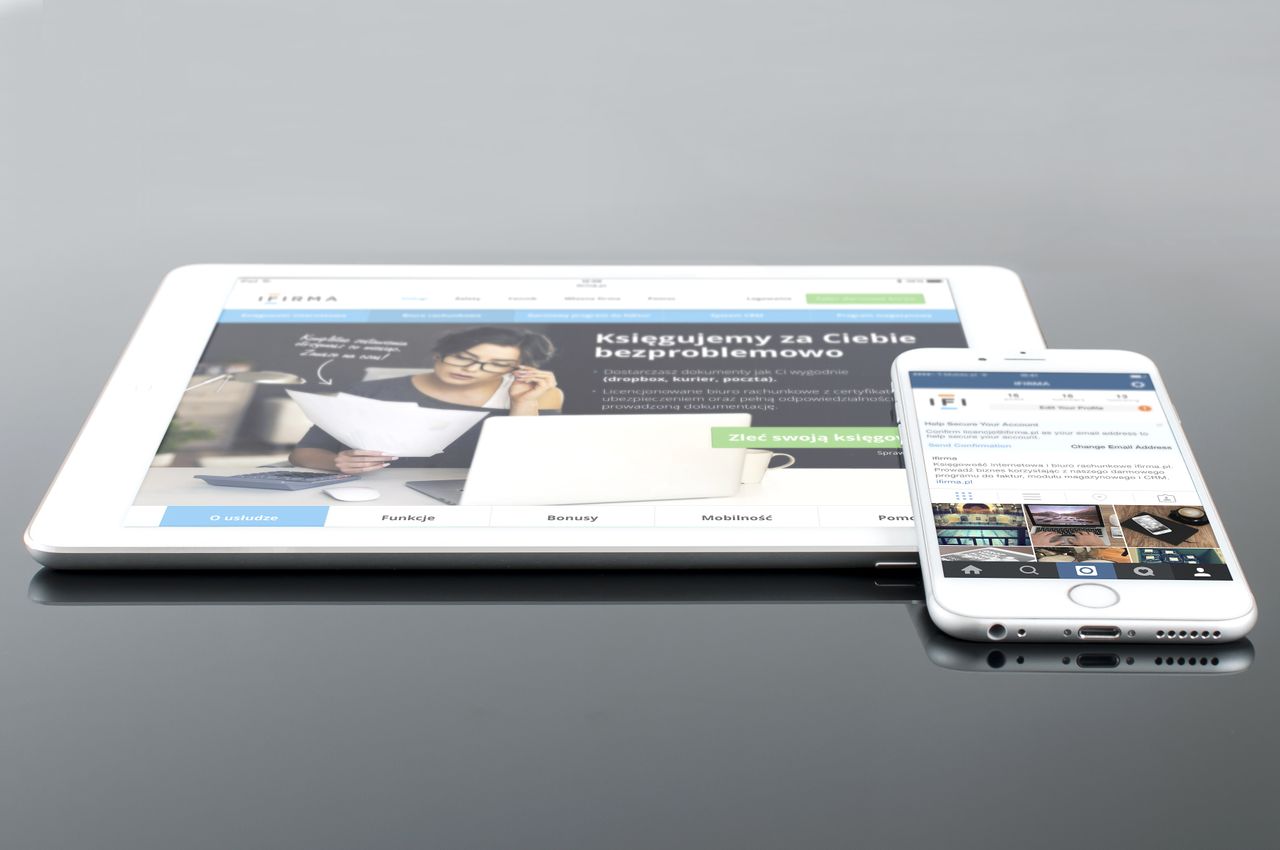 A modern tablet and smartphone showing web content on a glossy reflective surface, emphasizing technology and connectivity.