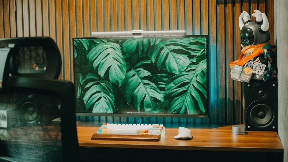 A smartphone rests on a wooden table beside a blurred laptop in a warm indoor setting.